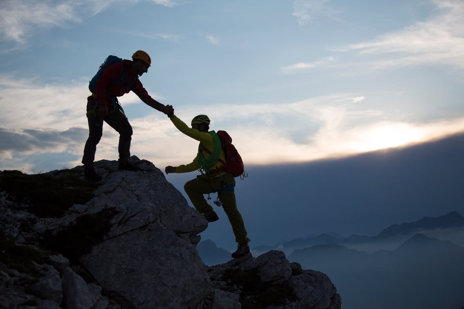 Two climbers helping each other up a ridge